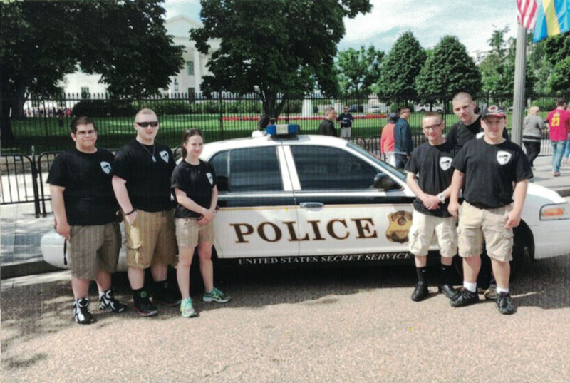 Junior shooting sports enthusiasts in front of a police car