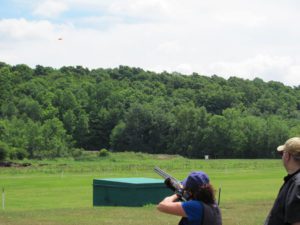Woman in a vest shooting a shotgun at a far distance