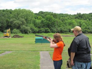 Woman in orange shooting a gun at an angle