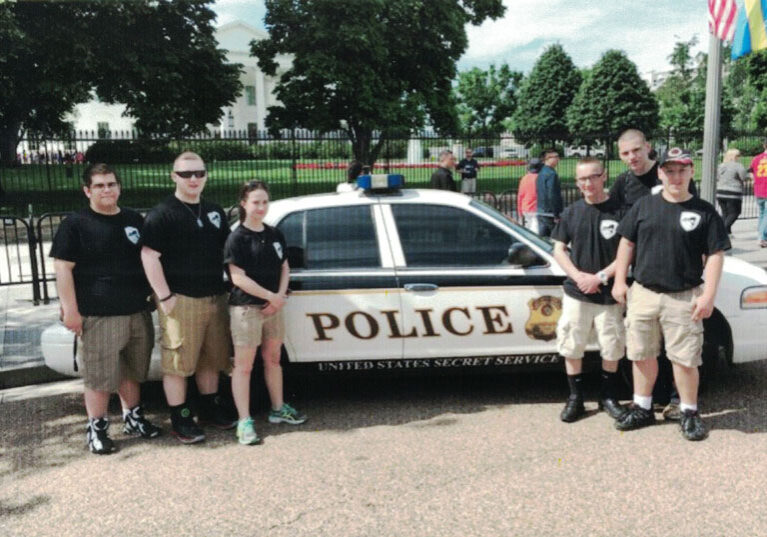 Junior shooting sports enthusiasts in front of a police car