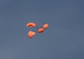 Four orange parachutes falling through clear sky